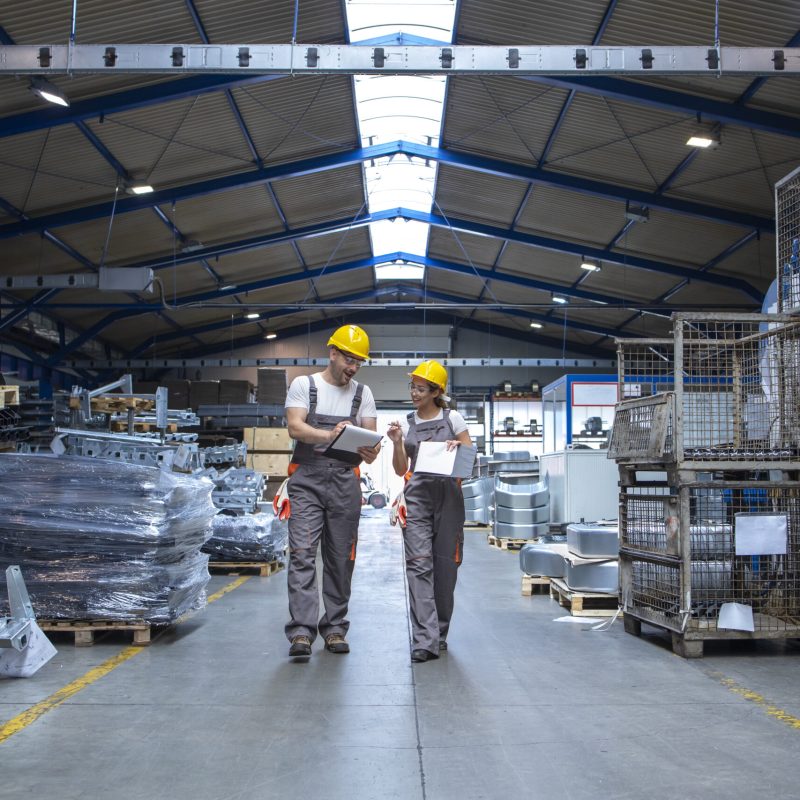 Factory workers walking through large production hall and having conversation.